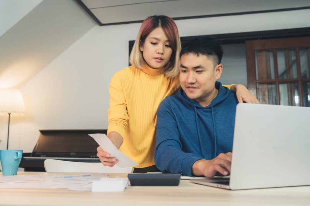 young-asian-couple-managing-finances-reviewing-their-bank-accounts-using-laptop-computer